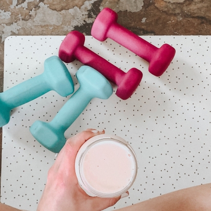 Legs folded on a yoga mate with weights and a protein shake