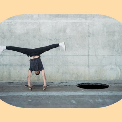 Photo of a man doing a handstand on a skateboard that is hurdling to a pitfall on the ground.