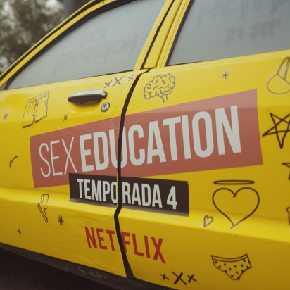 A yellow car seen from the side with a big logo on the side that says 'Sex Education'