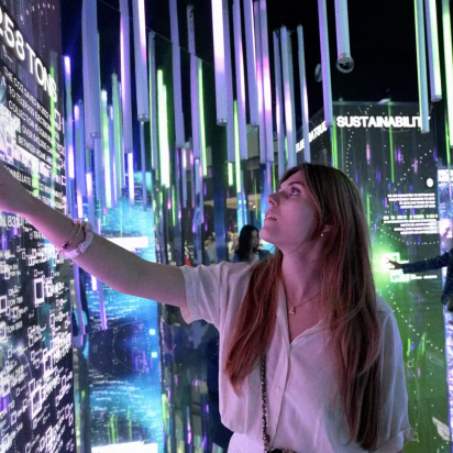 A women standing in front of a touch screen. On the screens there are many lines graphs and letters in different colours.