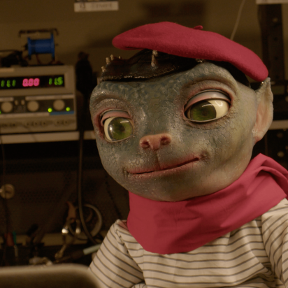 Image of Sir Martian, an animatronic in the form of an alien with large eyes and a cat-like nose. He wears an outfit befitting a Parisian street portrait artist.