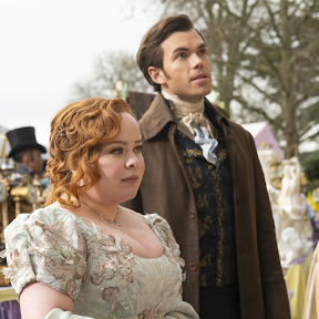 The image features a woman in a pastel dress and a man in a dark coat, sharing a moment of curiosity in a lively outdoor marketplace filled with vintage items and colorful tents.