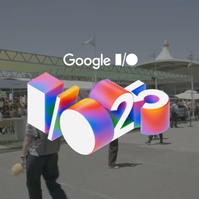 An outdoor shot of the Google I/O 2025 conference on a sunny day. In the foreground is a large, colorful, 3D graphic of the "I/O '25" logo. In the background, attendees walk between large white tents and event structures.