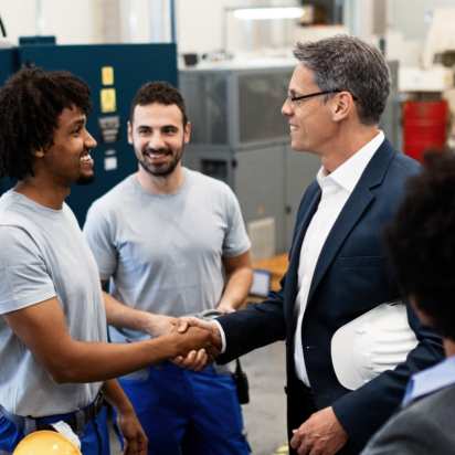 Businessmen shaking hands in a factory. Two factory workers and two people in suits are collaborating.