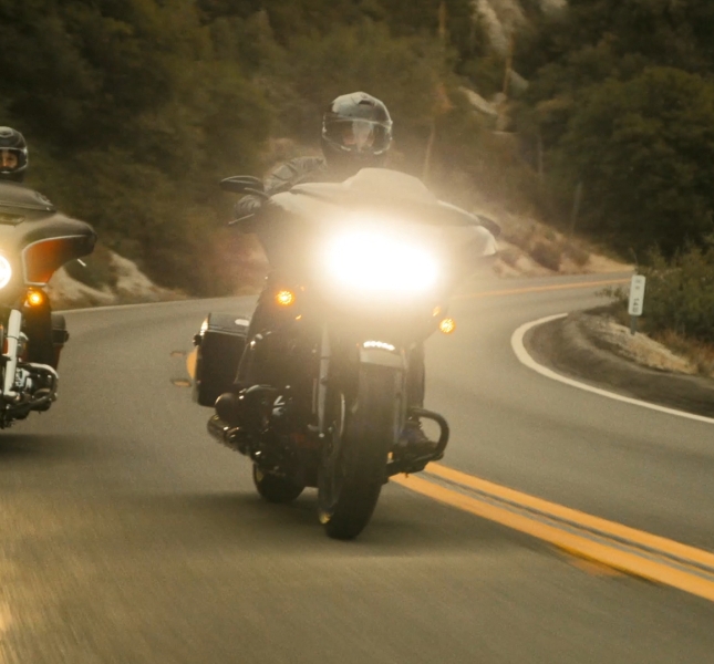 Two people riding Harley Davidson motorcycles down the road