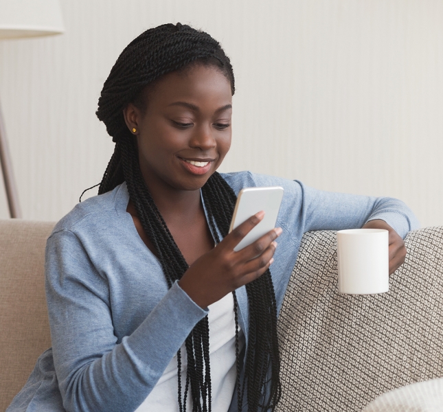 A person looking at their phone and enjoying a cup of coffee on the couch