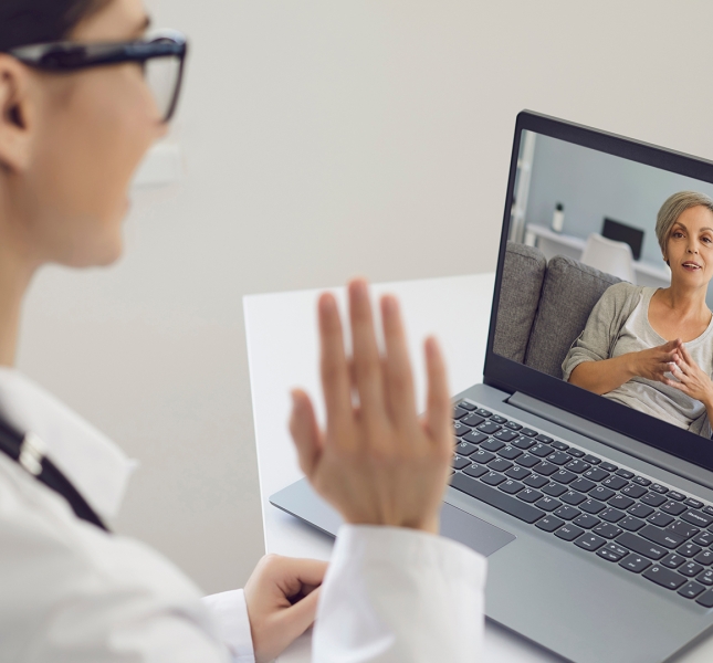 A doctor waiving to a patient via a laptop telehealth appointment