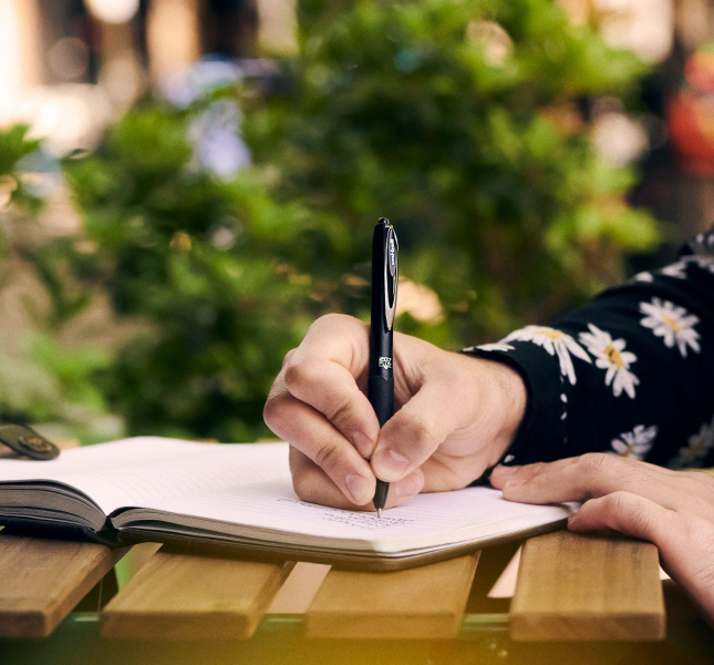 Someone writing in a notebook with a uni pen