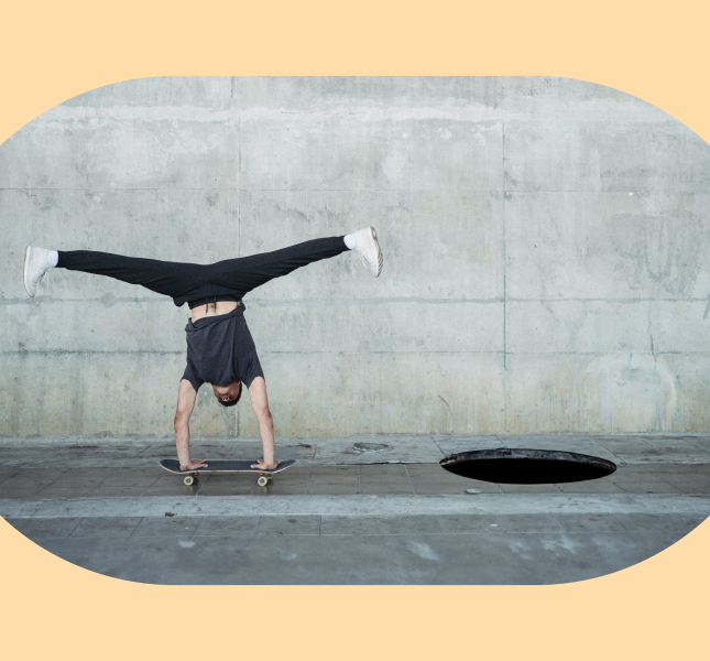 Photo of a man doing a handstand on a skateboard that is hurdling to a pitfall on the ground.