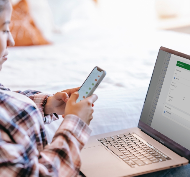 Young woman with a laptop on her lap and a mobile phone in her hand.