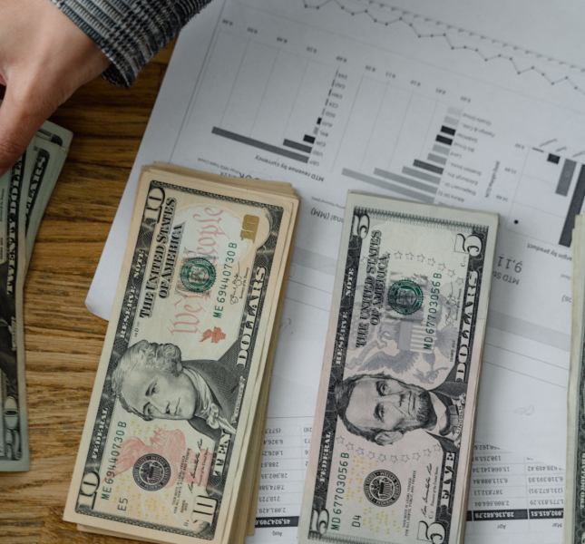 Four stacks of cash sitting atop a printout of different charts and graphs.