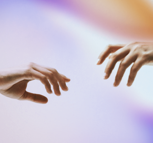 Two hands reaching towards each other with fingers slightly extended, set against a soft, gradient background of purple, blue, and orange hues. One hand has a black wristband.