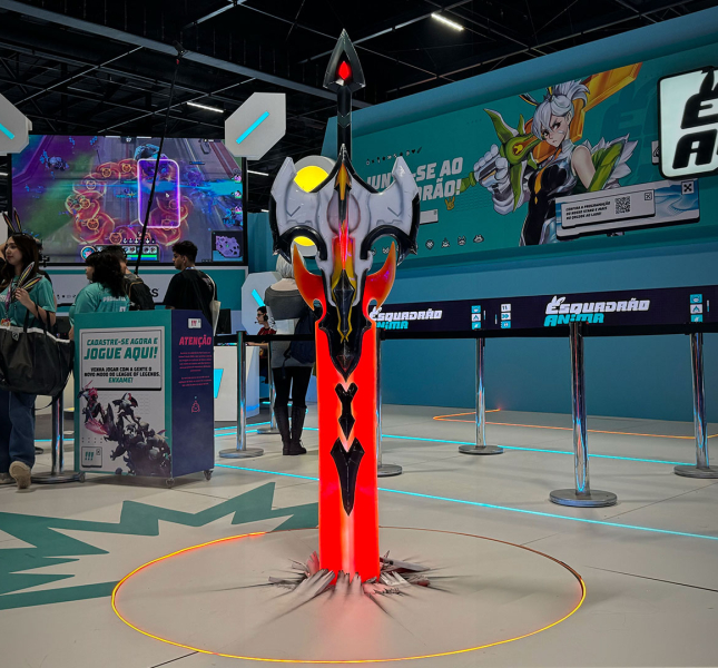 Events hall with a counter for Riot Games. In front of the counter there are people standing in line to have their picture taken with the installation. An axe that stands up straight and is painted in red and black.