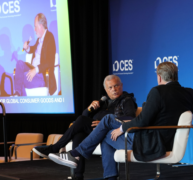 two men sitting on stage at CES with a screen showing them from a different angle in the background