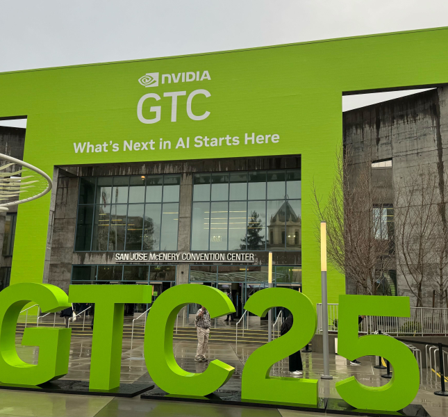 Green building facade that says "NVIDIA GTC: What's next in AI starts here." In the foreground is a sculpture of the hashtag "#GTC25."