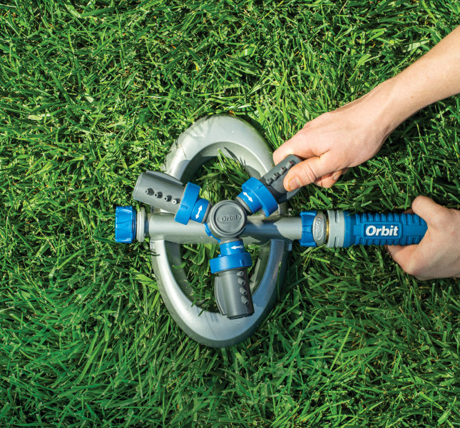 Hands turning on an Orbit sprinkler unit in a green lawn