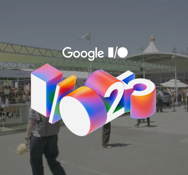 An outdoor shot of the Google I/O 2025 conference on a sunny day. In the foreground is a large, colorful, 3D graphic of the "I/O '25" logo. In the background, attendees walk between large white tents and event structures.