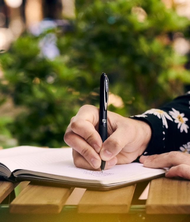 Someone writing in a notebook with a uni pen