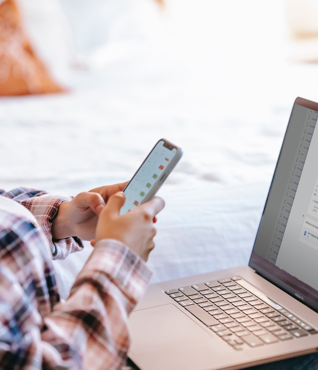 Young woman with a laptop on her lap and a mobile phone in her hand.