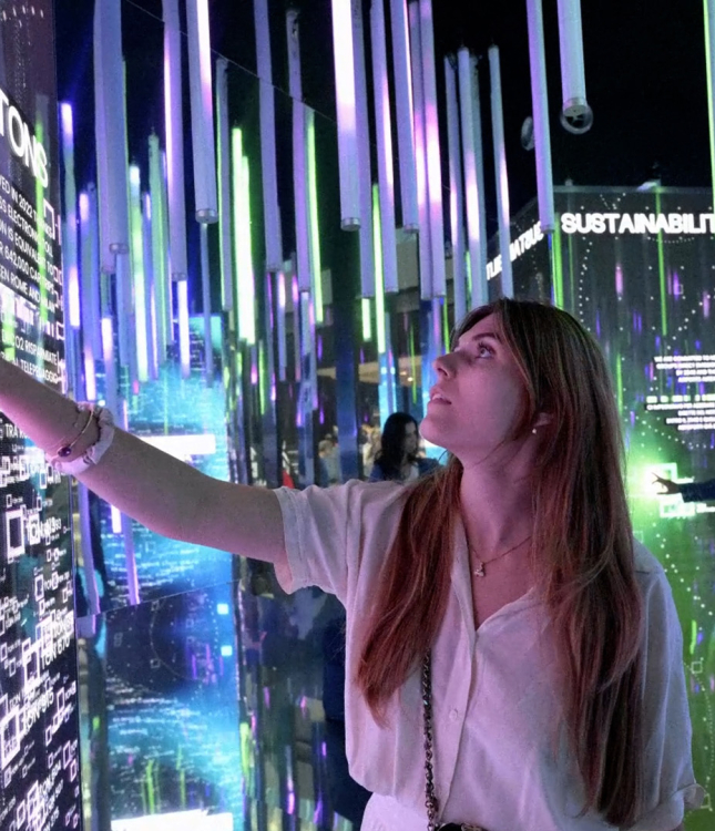 A women standing in front of a touch screen. On the screens there are many lines graphs and letters in different colours.