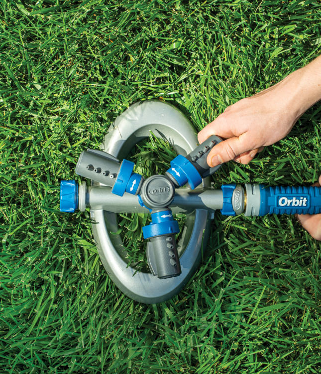 Hands turning on an Orbit sprinkler unit in a green lawn