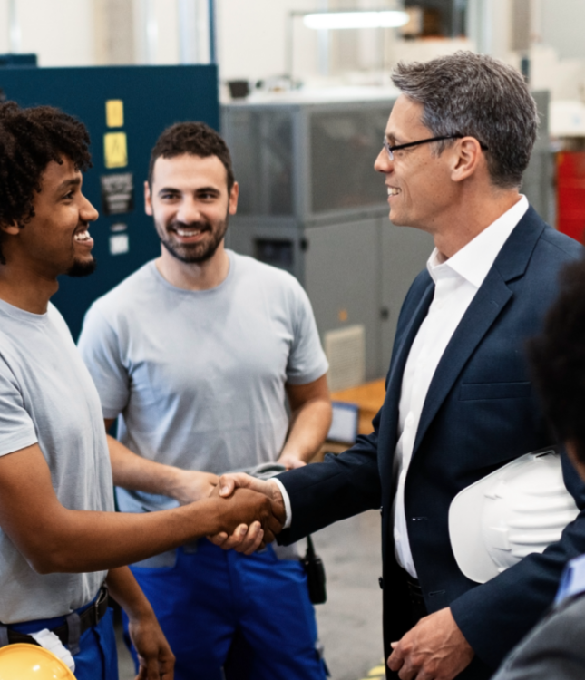 Businessmen shaking hands in a factory. Two factory workers and two people in suits are collaborating.