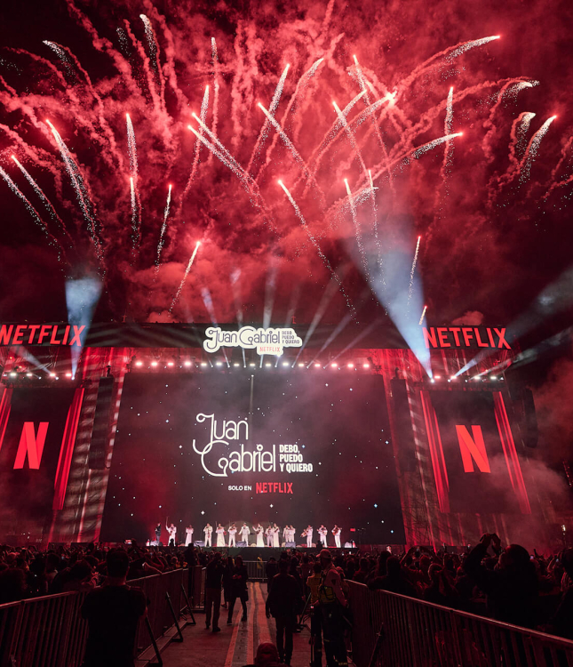 The massive stage for the Juan Gabriel Netflix screening in the Zócalo filled with fans. There are fireworks exploding in the background.
