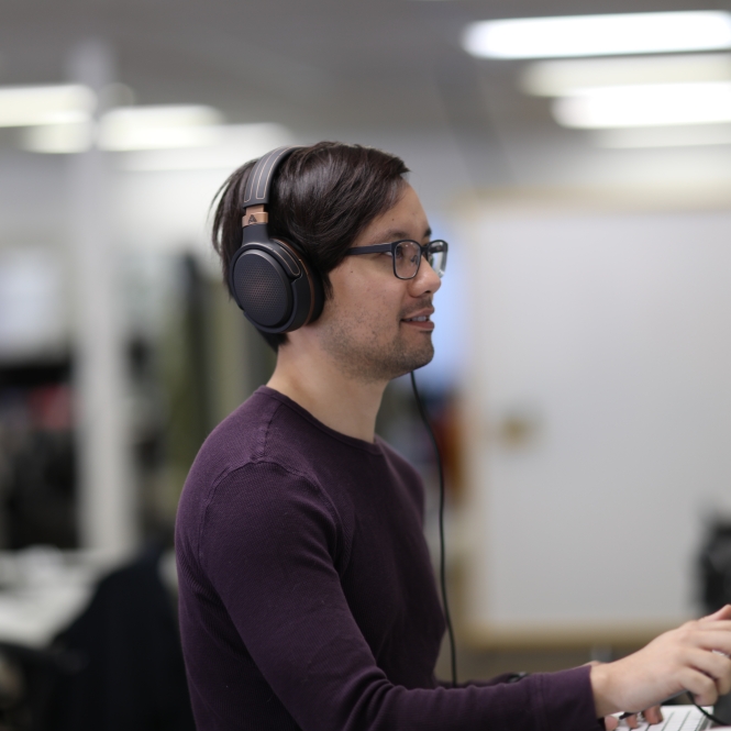 A person wearing headphones stands at their computer desk