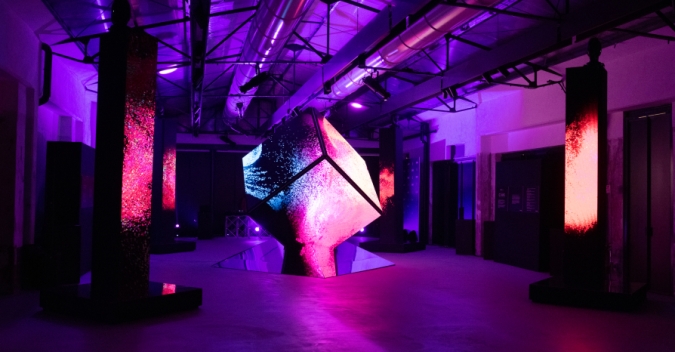 A large piece of art sitting inside of a building, lit. 'the cube'. It's a projection design installation. Masterpiece work of art