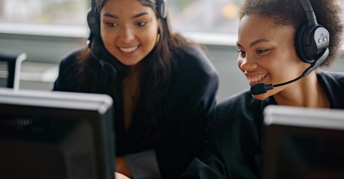 Two business women discussing a call over their desktop computers