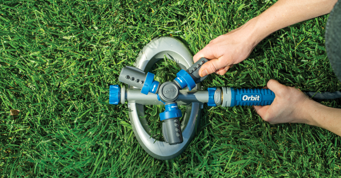 Hands turning on an Orbit sprinkler unit in a green lawn