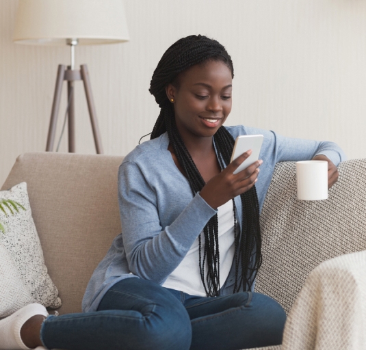 A person on their phone enjoying a cup of coffee on the couch