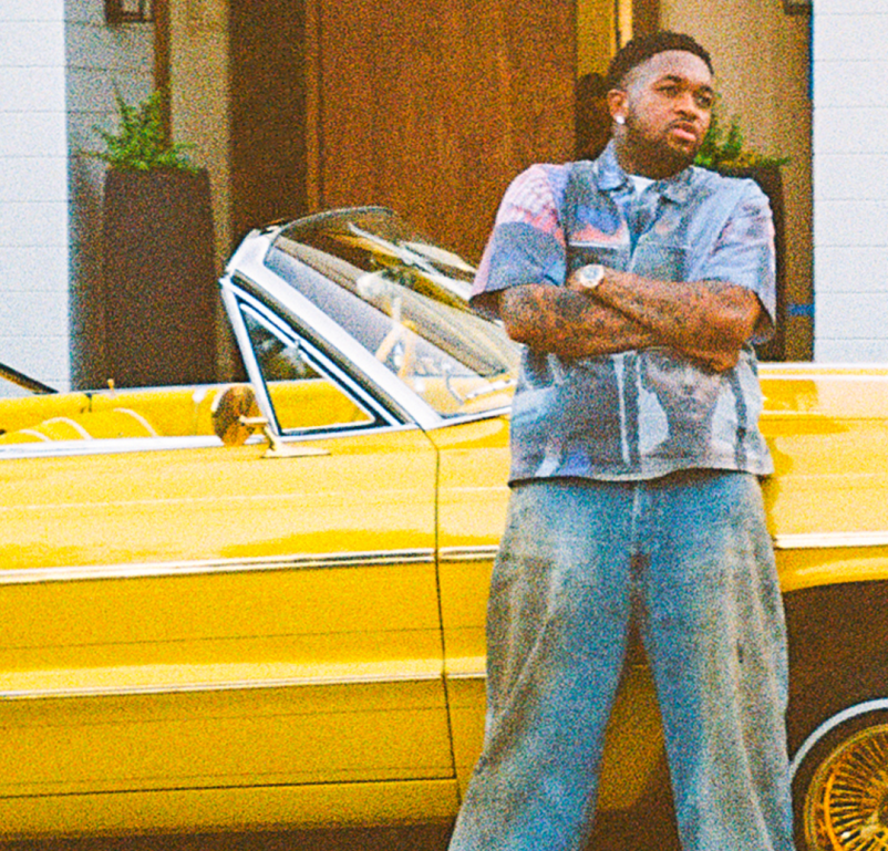 DJ Mustard, the brand collaborator, leaning against a vintage bright yellow low-rider convertible with gold wire wheels, capturing the vibrant, custom-culture aesthetic of the Heinz Mustaaaaard campaign.