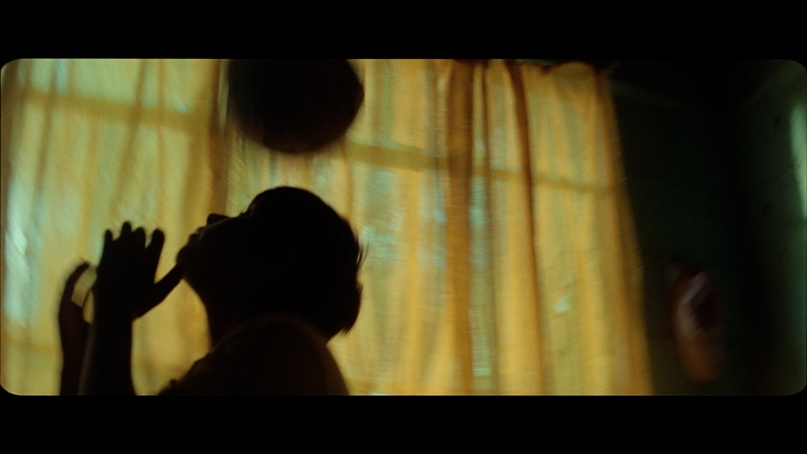 child playing with a ball, silhouetted against a yellow window curtain