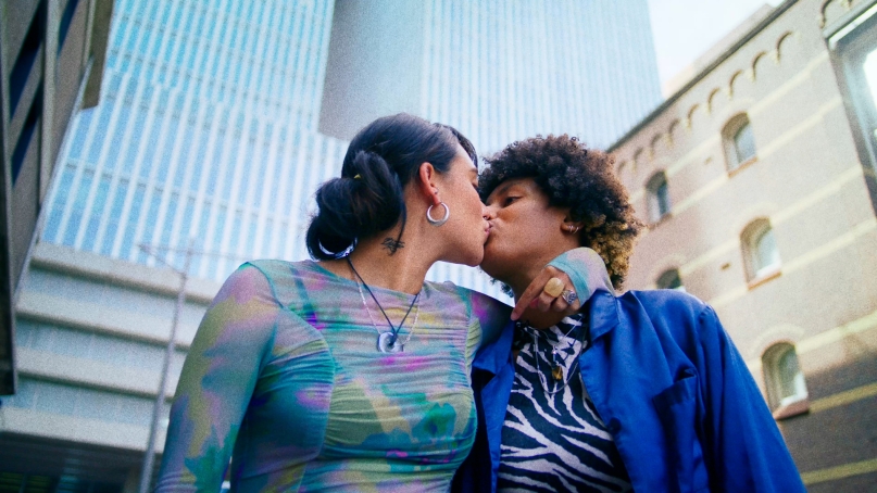 Two women in colorful outfits kissing, in a city setting