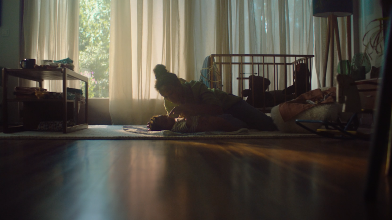 A women laying of the living room on the ground playing with her baby.