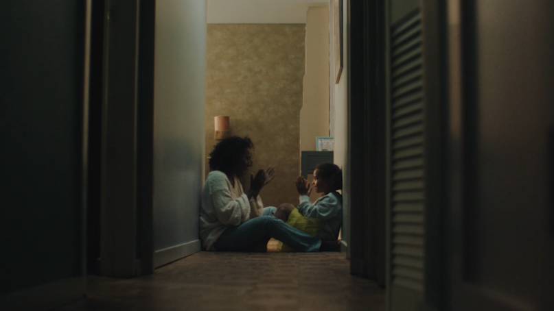 Women and child are sitting on the ground in a hallway. They are playing a game with clapping hands.