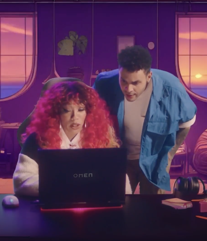 Women sitting on a couch looking at a laptop screen. A man looks at the same screen and is standing behind her.