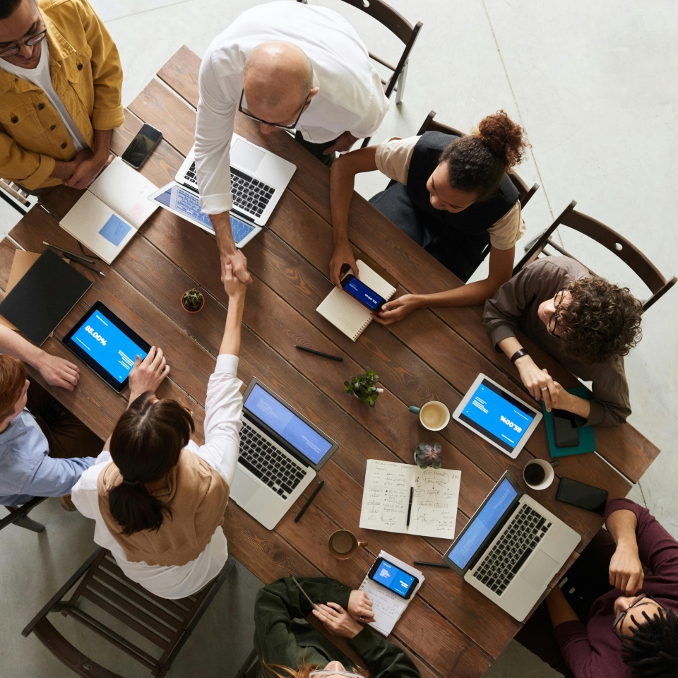 Table seen from above with people sitting around it and two people are shaking hands