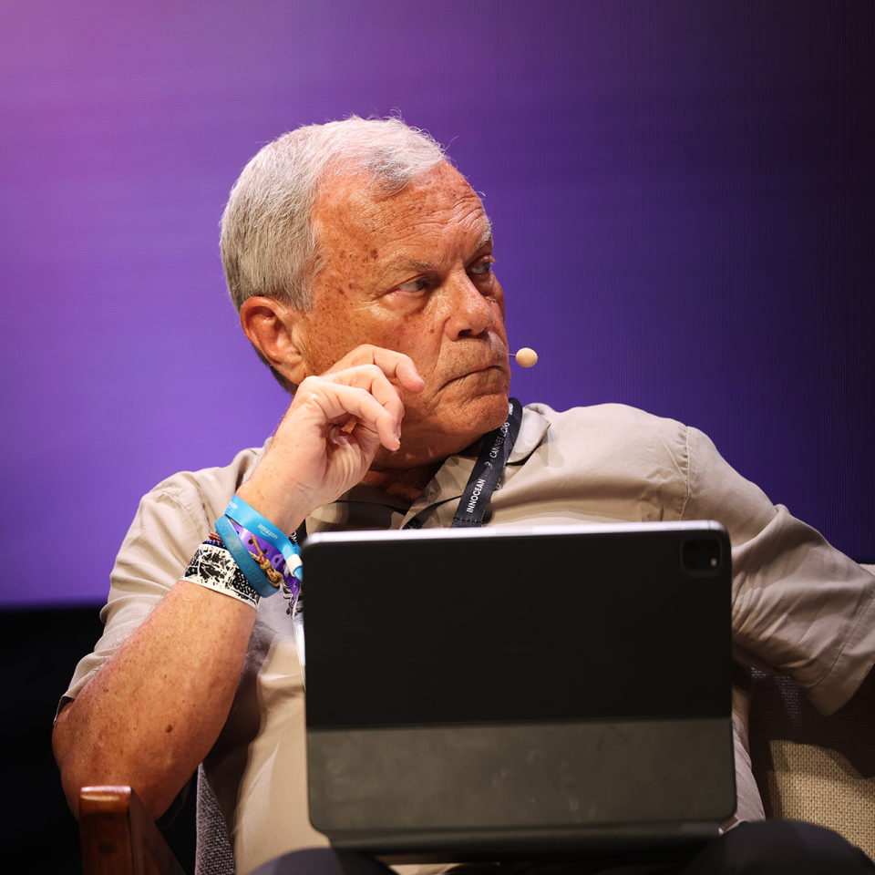 Sir Martin Sorrell speaking on stage with a ipad on his lap