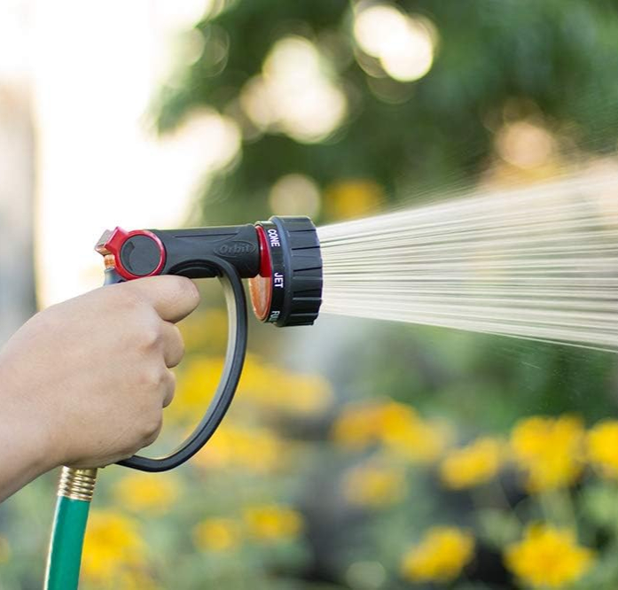 An Orbit hose being sprayed in a garden of yellow flowers