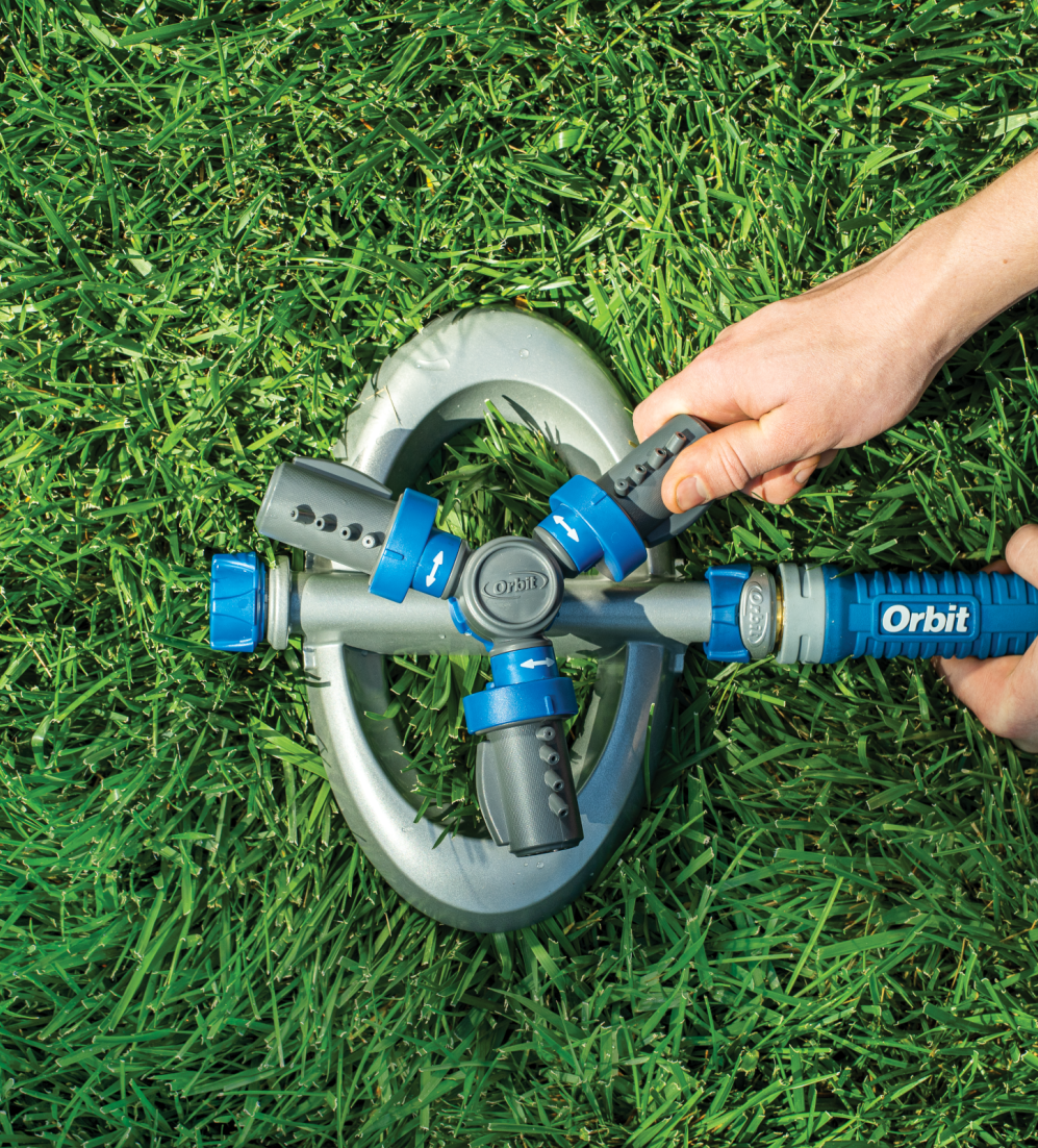Hands turning on an Orbit sprinkler unit in a green lawn