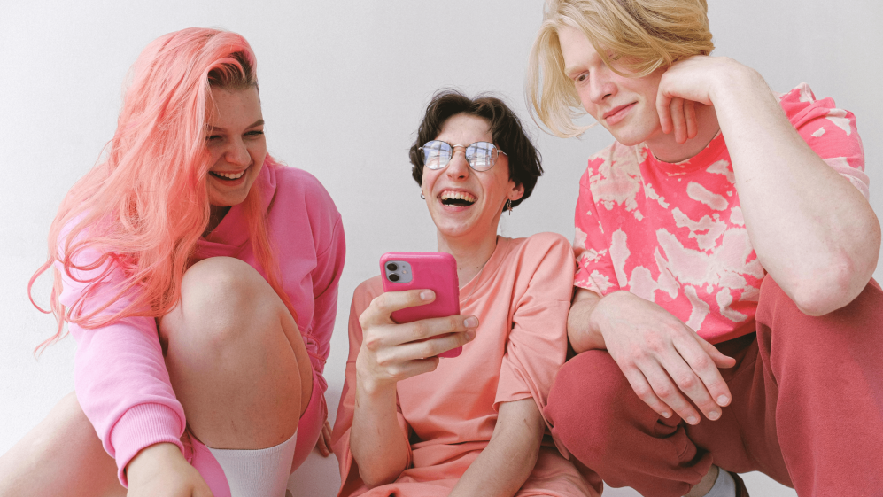 Three people dressed in neon pink laughing together in response to something on a phone