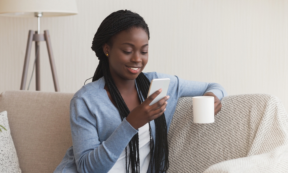 A person looking at their phone and enjoying a cup of coffee on the couch