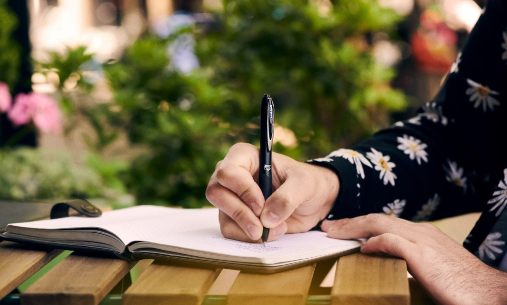 Someone writing in a notebook with a uni pen