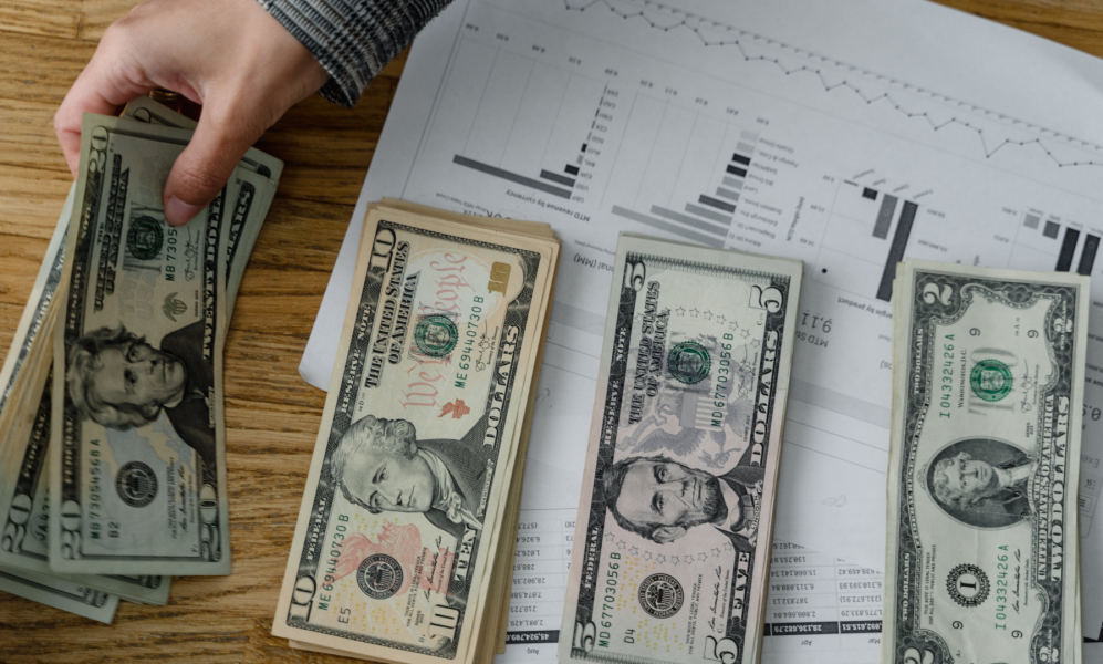 Four stacks of cash sitting atop a printout of different charts and graphs.