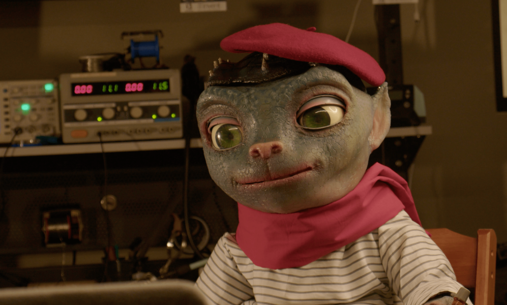Image of Sir Martian, an animatronic in the form of an alien with large eyes and a cat-like nose. He wears an outfit befitting a Parisian street portrait artist.