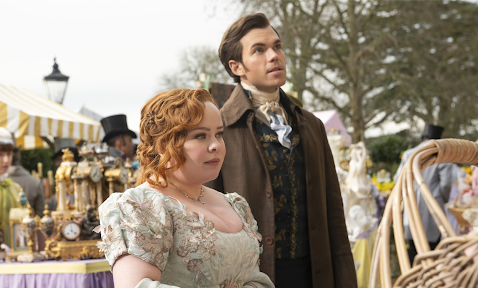 The image features a woman in a pastel dress and a man in a dark coat, sharing a moment of curiosity in a lively outdoor marketplace filled with vintage items and colorful tents.