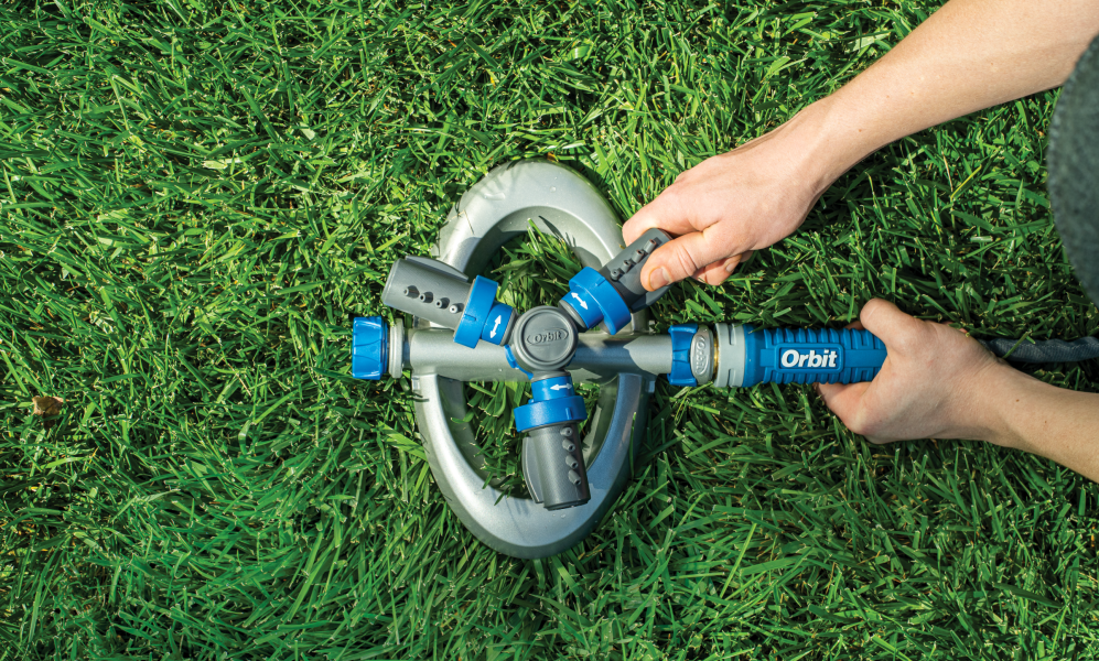 Hands turning on an Orbit sprinkler unit in a green lawn