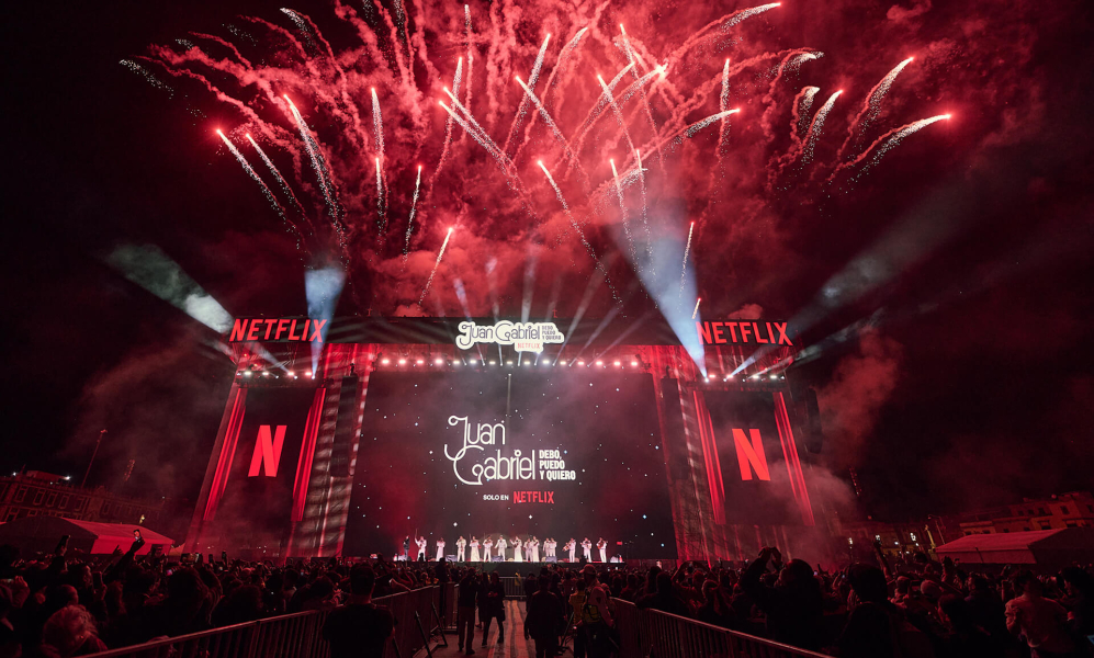 The massive stage for the Juan Gabriel Netflix screening in the Zócalo filled with fans. There are fireworks exploding in the background.